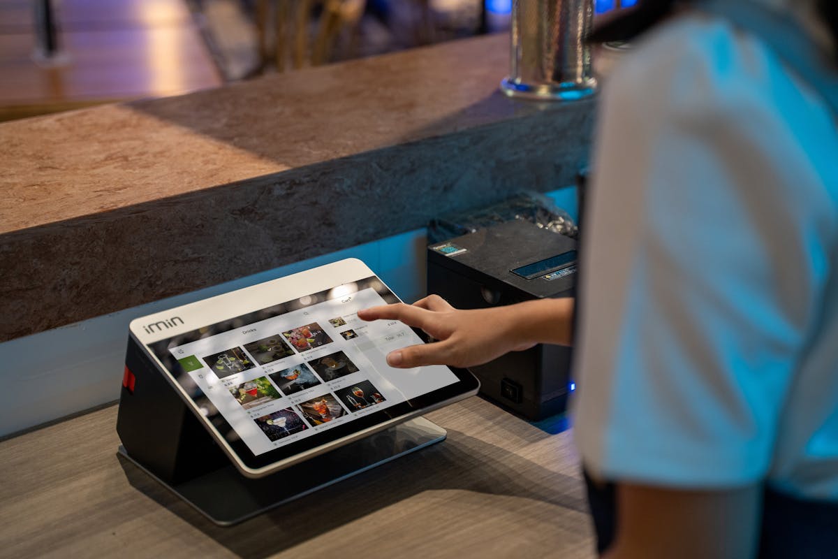 Restaurant staff using a touchscreen ordering system at a counter.